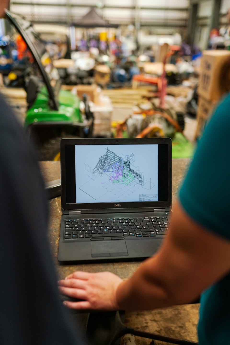 Two people reviewing engineering plans on a laptop in a workshop.
