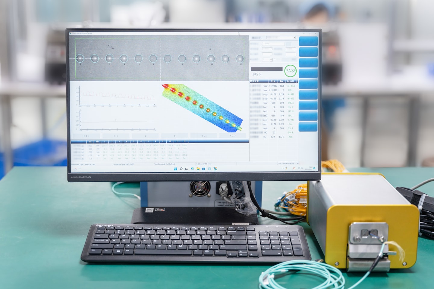 Computer monitor displays technical graphs connected to industrial machinery on a workbench.